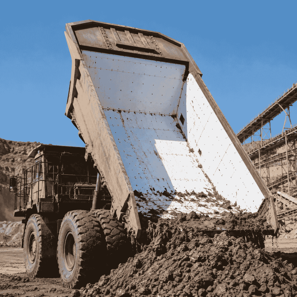 Mining dump truck unloading wet material from a raised bed lined with white UHMWPE wear-resistant sheets.